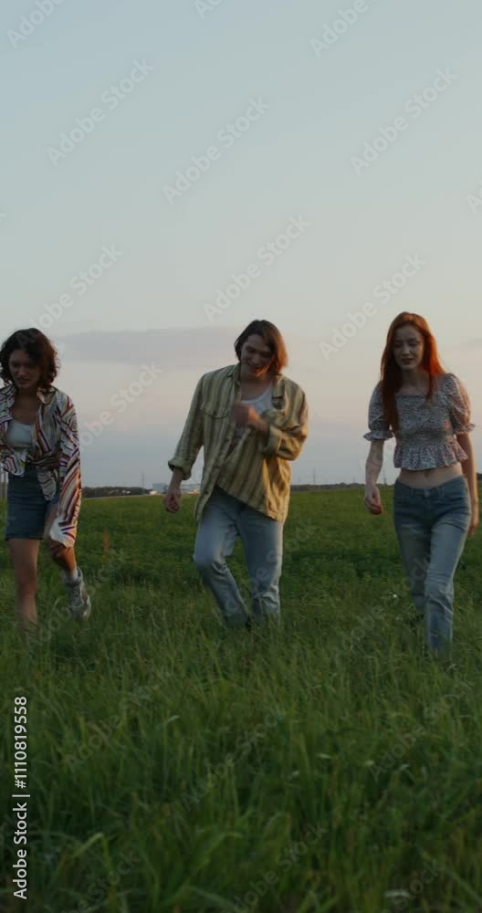Three young people are talking and smiling while walking in a field on a summer day Three young people are talking and smiling while walking in a field on a summer day
