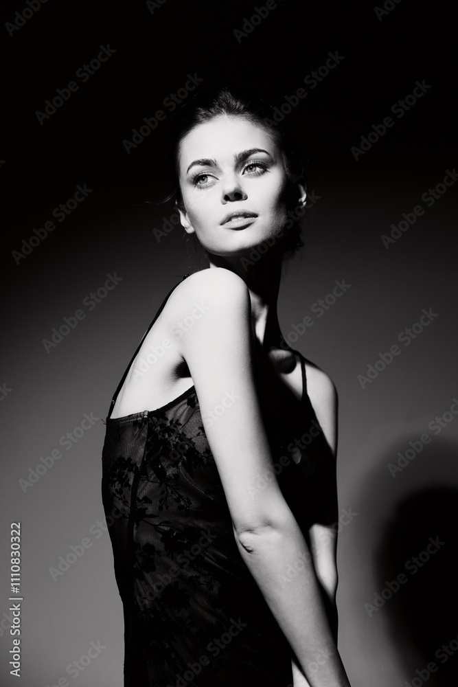 Elegant woman in a black dress posing gracefully against a dark background, showcasing confidence and poise with a soft expression. Fashion and beauty concept.