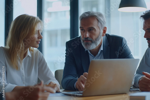 A business meeting with three professionals discussing ideas around a laptop.