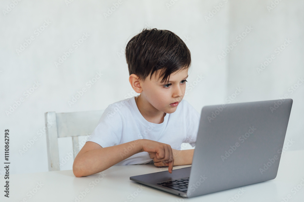 Little boy learning to play on laptop online at table Little boy learning to play on laptop online at table