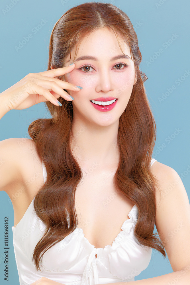 Pretty Asian beauty woman curly long hair with Korean makeup glowing face and healthy facial skin portrait smile on isolated blue background. Pretty Asian beauty woman curly long hair with Korean makeup glowing face and healthy facial skin portrait smile on isolated blue background.