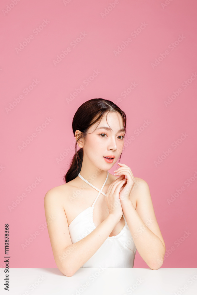 Young Asian woman gathered in ponytail with natural makeup on face have plump lips and clean fresh skin wearing white camisole on isolated pink background. Portrait of cute female model in studio. Young Asian woman gathered in ponytail with natural makeup on face have plump lips and clean fresh skin wearing white camisole on isolated pink background. Portrait of cute female model in studio.
