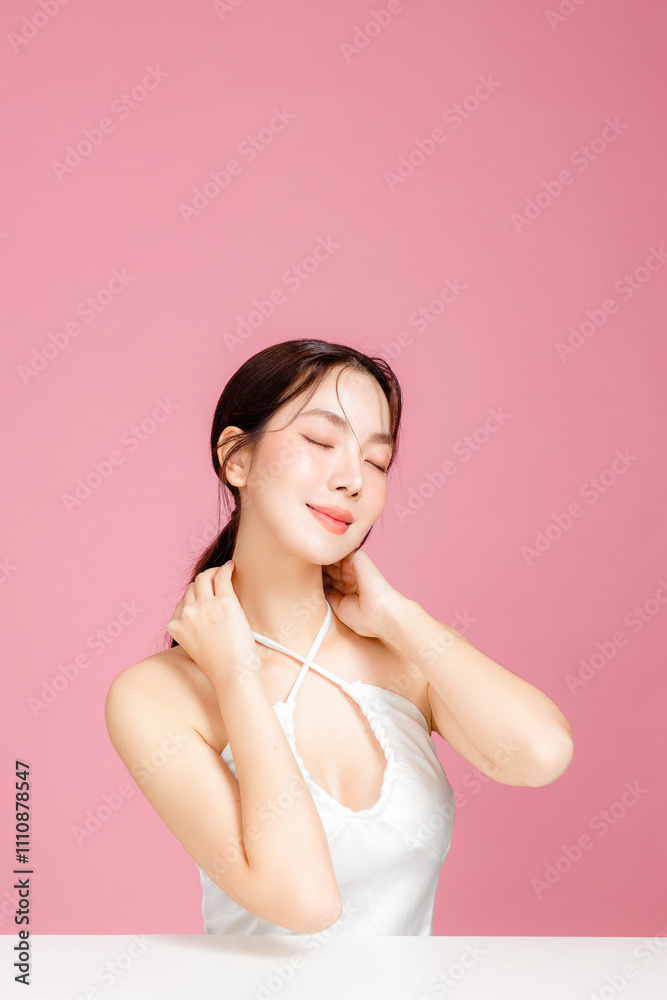 Young Asian woman gathered in ponytail with natural makeup on face have plump lips and clean fresh skin wearing white camisole on isolated pink background. Portrait of cute female model in studio. Young Asian woman gathered in ponytail with natural makeup on face have plump lips and clean fresh skin wearing white camisole on isolated pink background. Portrait of cute female model in studio.