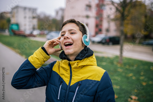 A young boy walking down a city street, wearing headphones and dressed in warm winter clothing