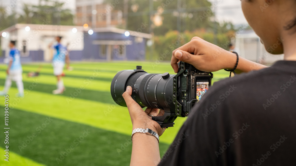 A photographer documenting a mini soccer game using a telephoto lens, focusing on players on a well-maintained green field under natural light, capturing dynamic sports moments