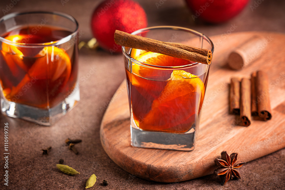 Portion of winter traditional red mulled wine drink or hot christmas punch with orange citrus slices served in glass with cinnamon stick on wooden board dark brown table with spices for holiday Portion of winter traditional red mulled wine drink or hot christmas punch with orange citrus slices served in glass with cinnamon stick on wooden board dark brown table with spices for holiday