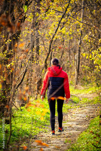 A middle-aged woman makes her way along a winding forest path, surrounded by the rich hues of autumn. Her sturdy backpack and trekking poles reflect a deep passion for adventure.