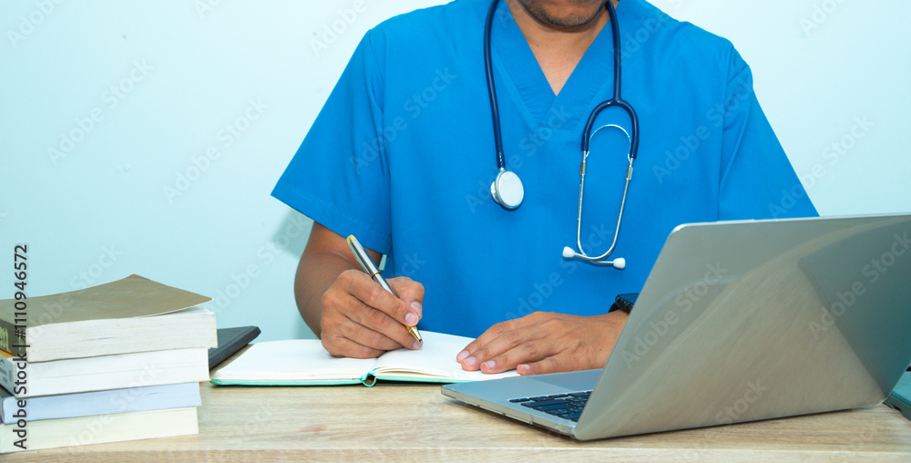 Smart medicine doctor working with computer notebook and medical text book at desk in the hospital.The physician, in the blue medical coat is filling out a medical record form.Medical concept Smart medicine doctor working with computer notebook and medical text book at desk in the hospital.The physician, in the blue medical coat is filling out a medical record form.Medical concept