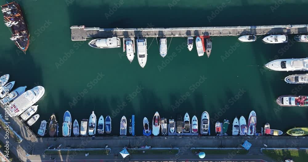 Top-down drone perspective of Batumi’s marina, with rows of yachts and boats anchored against the shimmering Black Sea waters. Top-down drone perspective of Batumi’s marina, with rows of yachts and boats anchored against the shimmering Black Sea waters.