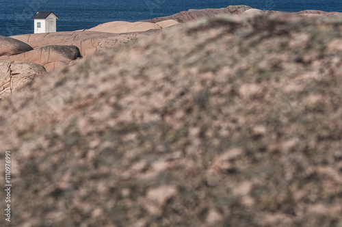 Small white structure on rocky coastline overlooking the blue ocean at midday under clear skies photo