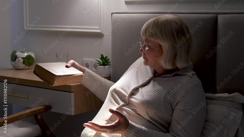 Elderly woman prepares for bed by placing book and glasses on nightstand, creating peaceful and cozy atmosphere for restful night. Closes classic book and takes off glasses. Closes eyes while resting