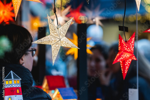 Besucher auf einem Weihnachtsmarkt vor einem Satand mit leuchtenden Sternen zum Verkauf photo