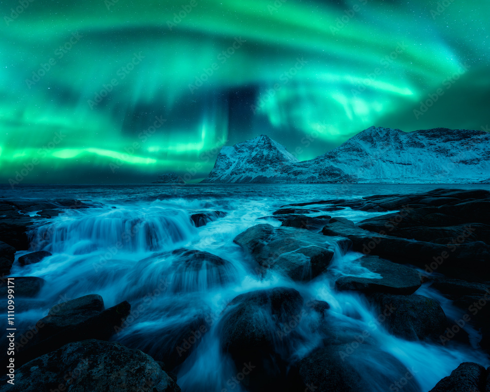 Naklejka premium Aurora borealis on night starry sky, rocky shore with stones in water in winter. Landscape with northern lights, fjord, beach, sea and snowy mountains in Lofoten Islands, Norway. Polar lights
