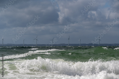 Wind turbines standing offshore with rough and choppy waves in the foreground