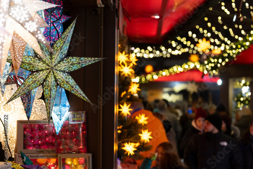 Besucher auf einem Weihnachtsmarkt vor einem Stand mit leuchtenden Sternen photo