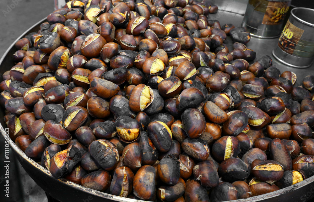 Obraz premium Roasted chestnuts cooked in a large metal pan for sale at a street food stall