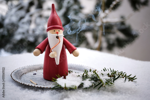 Handmade Santa Claus smoking figurine, traditional German Christmas decoration from the Erzgebirge in East Germany. Shot outdoors on a cold snowy winter morning.