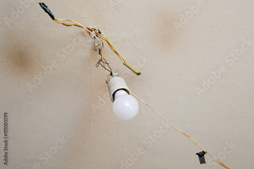 exposed lightbulb fixture hanging from ceiling connected by exposed somewhat precarious wiring home repair DIY safely fixing upgrading electrical fixtures professional installation minimalism  photo