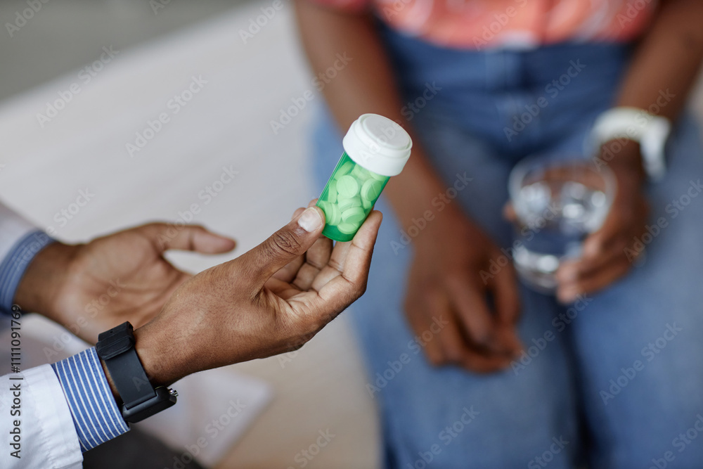 Close up of unrecognizable African American doctor holding green pill bottle while explaining medication side effects to patient during consultation in clinic, copy space Close up of unrecognizable African American doctor holding green pill bottle while explaining medication side effects to patient during consultation in clinic, copy space