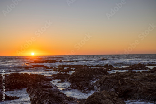 Sunset on a Pacific Ocean beach, rocky shoreline with seaweed and driftwood, nobody	