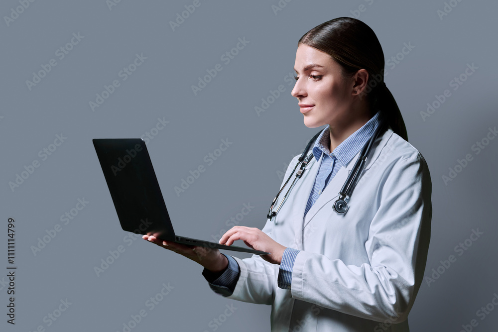 Profile portrait of female doctor using laptop on gray background Profile portrait of female doctor using laptop on gray background