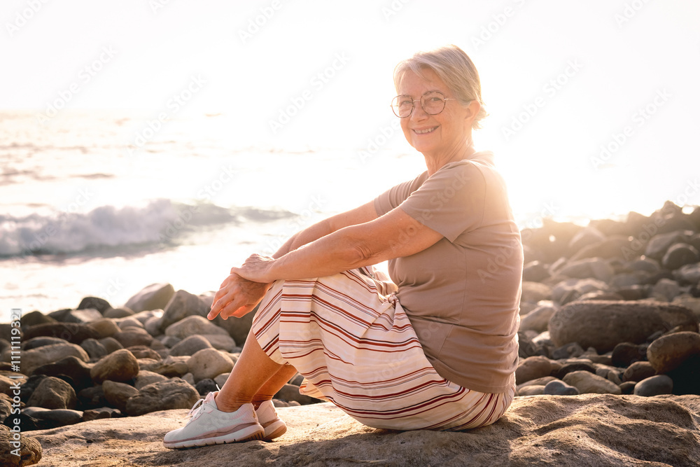 Φωτογραφία Portrait of attractive relaxed senior woman sitting at the beach at sunset looki
