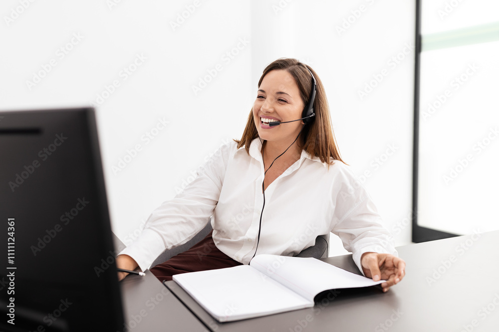 A Caucasian businesswoman sits at her desk, wearing a headset and engaging in a virtual meeting. She appears focused and cheerful as she interacts with colleagues on her computer. A Caucasian businesswoman sits at her desk, wearing a headset and engaging in a virtual meeting. She appears focused and cheerful as she interacts with colleagues on her computer.