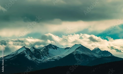 Peaks rise majestically, their snow covered slopes contrasting against dark, swirling clouds, capturing natures raw beauty in a serene, atmospheric landscape.