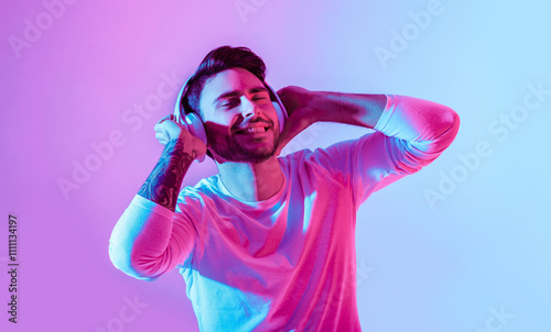 Relax with favorite music. Man in big wireless headphones closes eyes and enjoys song, isolated in neon, studio shot photo