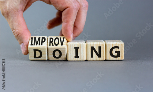 Doing or improving symbol. Businessman turns wooden cubes and changes the word Doing to Improving. Beautiful grey table grey background. Educational business doing or improving concept. Copy space.