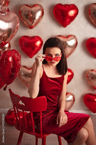 Stylish woman in a red dress and heart-shaped sunglasses posing with romantic balloons
