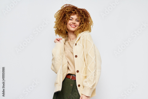 Happy young woman with curly hair wearing a cozy beige sweater against a light gray background, smiling confidently Perfect for fashion and lifestyle themes photo