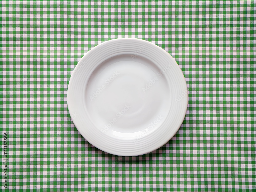 A simplistic, empty white plate sits at the center of a vivid green checkered tablecloth, inviting the viewer to imagine delicious dishes and gatherings A simplistic, empty white plate sits at the center of a vivid green checkered tablecloth, inviting the viewer to imagine delicious dishes and gatherings