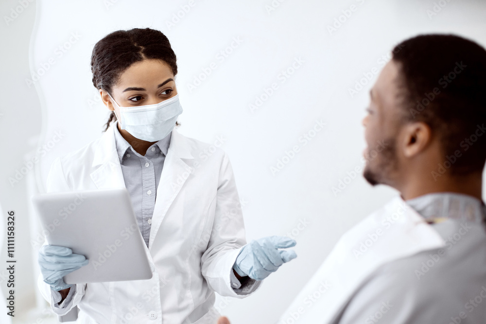 Stomatologist Woman With Digital Tablet In Hands Consulting Male Patient In Clinic, African American Stomatologist Woman In Medical Mask Explaining Teeth Treatment Process To Young Man, Closeup Stomatologist Woman With Digital Tablet In Hands Consulting Male Patient In Clinic, African American Stomatologist Woman In Medical Mask Explaining Teeth Treatment Process To Young Man, Closeup