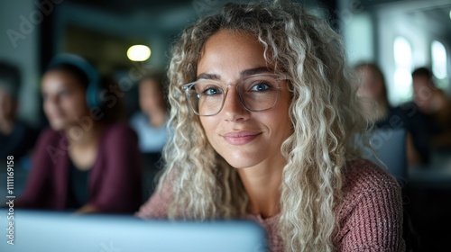 A woman with curly hair and glasses looks contently at her screen, exuding calm and focus in a contemporary social or academic environment, feeling connected.