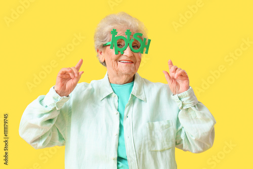 Happy senior woman in plastic glasses for St. Patrick's Day celebration on yellow background photo