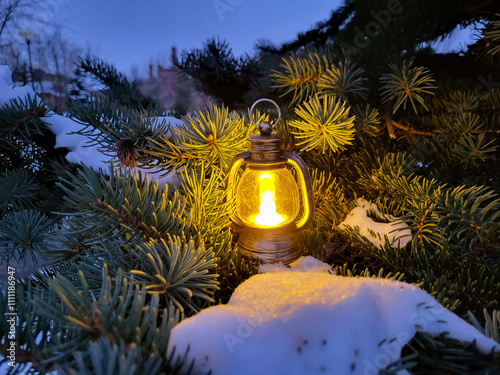 A glowing small decorative lantern stands in the snow on the branches of a fir tree. The concept of New Year and Christmas.
