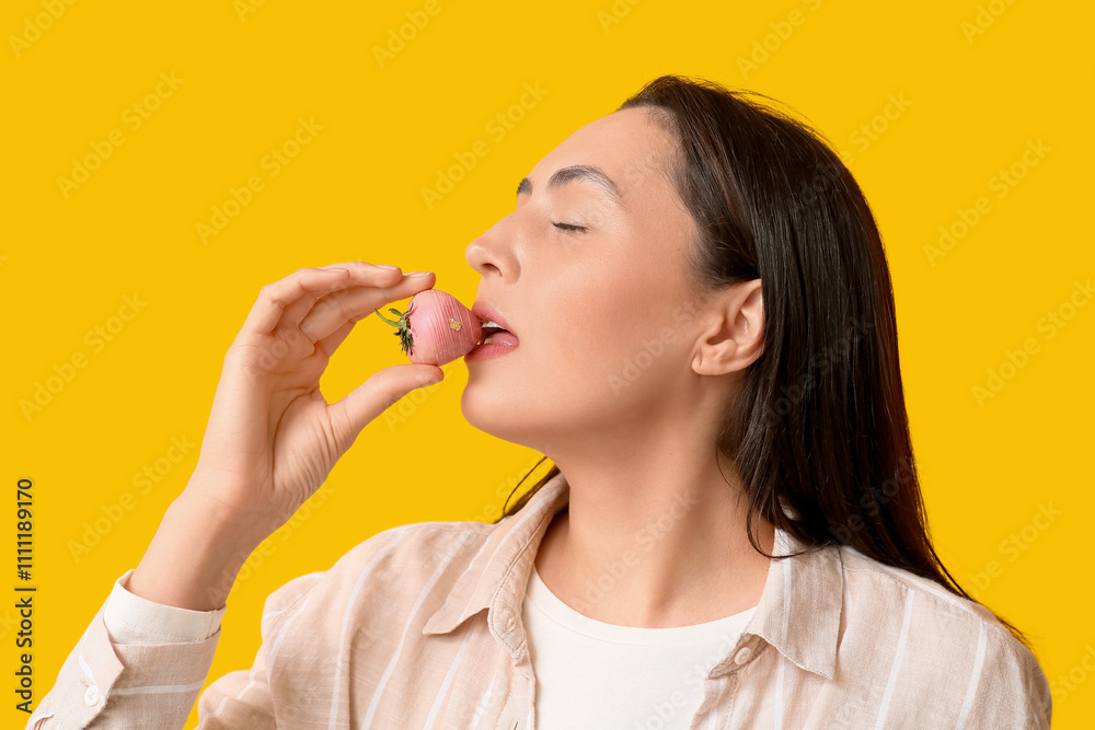 Beautiful young woman eating chocolate covered strawberry on yellow background Beautiful young woman eating chocolate covered strawberry on yellow background