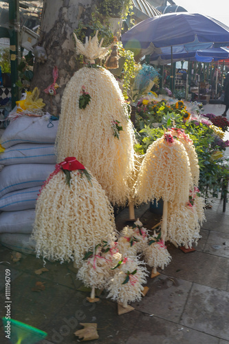 A market scene in Tbilisi where Christmas trees, festive branches, and traditional Georgian chichilaki decorative wood sculptures are displayed for sale. This image captures the holiday shopping photo