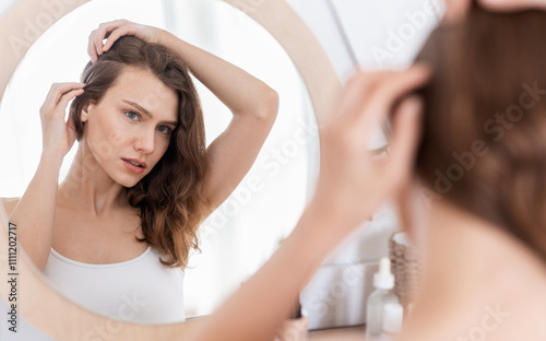 Hairloss concept. Young woman checking for thinning hair in mirror at home