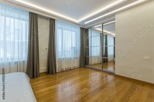 A spacious bedroom with parquet floors, large windows and a mirrored wardrobe.