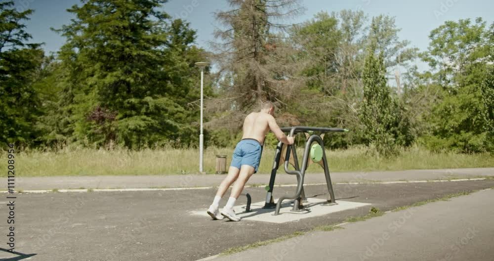 A muscular man performs push-ups in a park on a sunny day. He is working on his upper body strength and fitness routine.