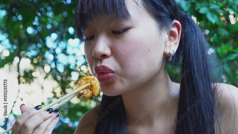 young cheerful asian woman eating fried hot shrimp with chopsticks in outdoor cafe, woman having seafood lunch in outdoor restaurant in park, close-up young cheerful asian woman eating fried hot shrimp with chopsticks in outdoor cafe, woman having seafood lunch in outdoor restaurant in park, close-up