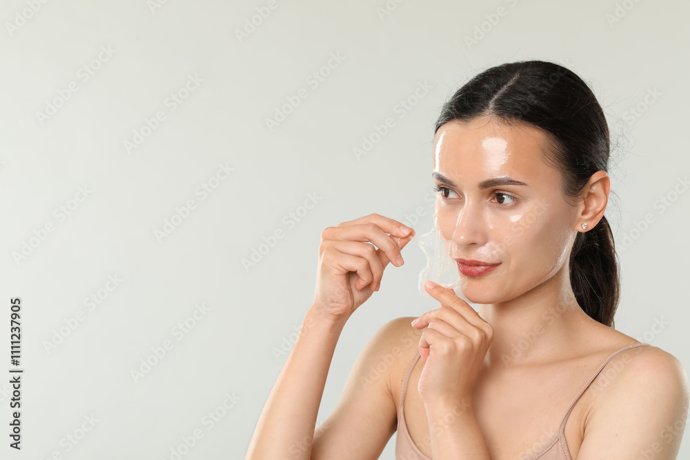 Beautiful woman peeling off face mask on light grey background. Space for text Beautiful woman peeling off face mask on light grey background. Space for text