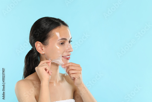 Smiling woman peeling off face mask on light blue background. Space for text