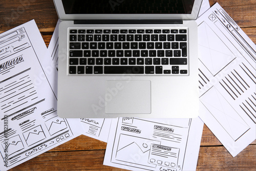 Developing UI design. Sketches of website wireframes and laptop on wooden table, top view photo