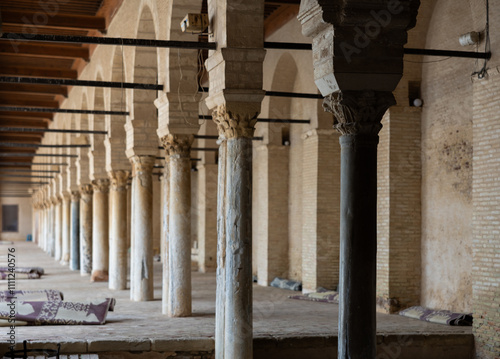 Perspective and narrow corridors of courtyard patio in Tunisian Grand Mosque of Kairouan. Rolled-up prayer mats lie in neat piles. religious building for Muslim believers photo