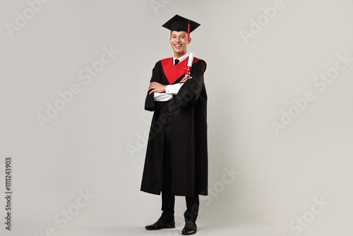 Happy student with diploma after graduation on grey background photo