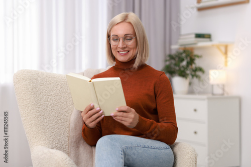 Portrait of smiling middle aged woman reading book on armchair at home