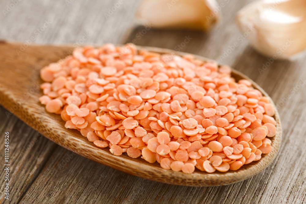 Raw dried red lentils split in halves on wooden spoon, garlic cloves in the back (Selective Focus, Focus one third into the lentils) Raw dried red lentils split in halves on wooden spoon, garlic cloves in the back (Selective Focus, Focus one third into the lentils)